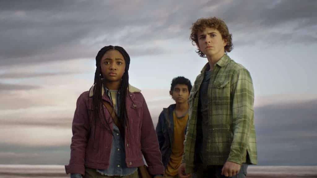From left to right: Leah Sava Jeffries as Annabeth Chase, Aryan Simhadri as Grover Underwood and Walker Scobell as Percy Jackson. Stood against a dark background and looking in the direction of the camera.