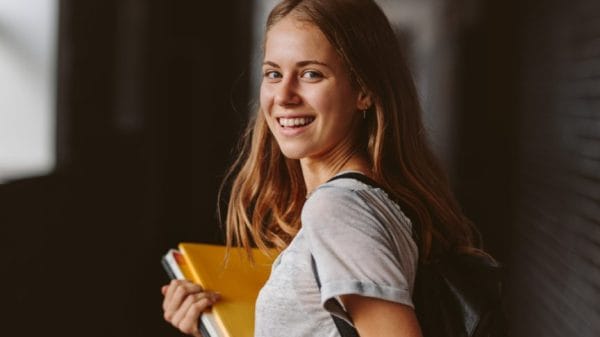 College student female with in teeshirt book in hands smiling