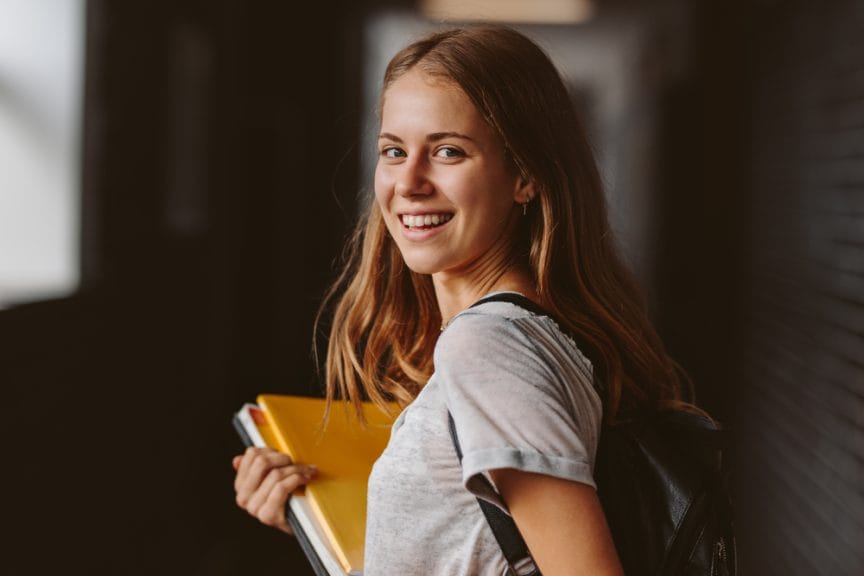 College student female with in teeshirt book in hands smiling