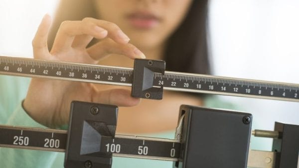 Midsection of mid adult Asian woman adjusting balance weight scale