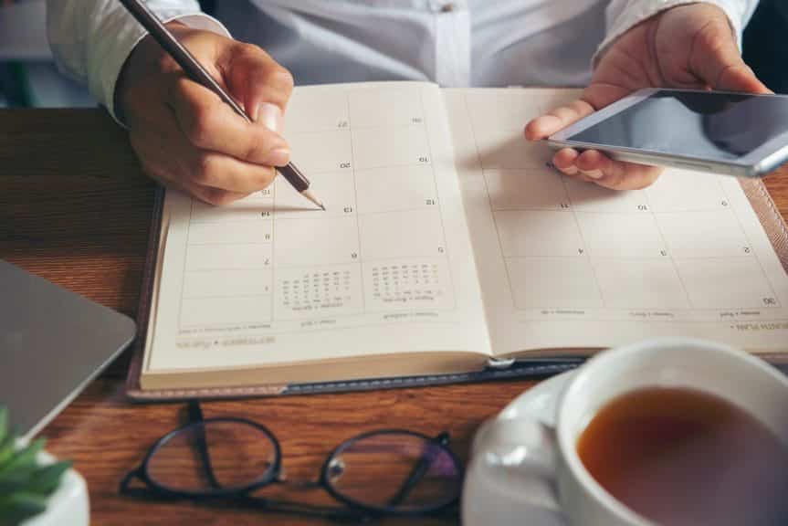 Women hand planning daily appointment and write business trip in diary at office desk.