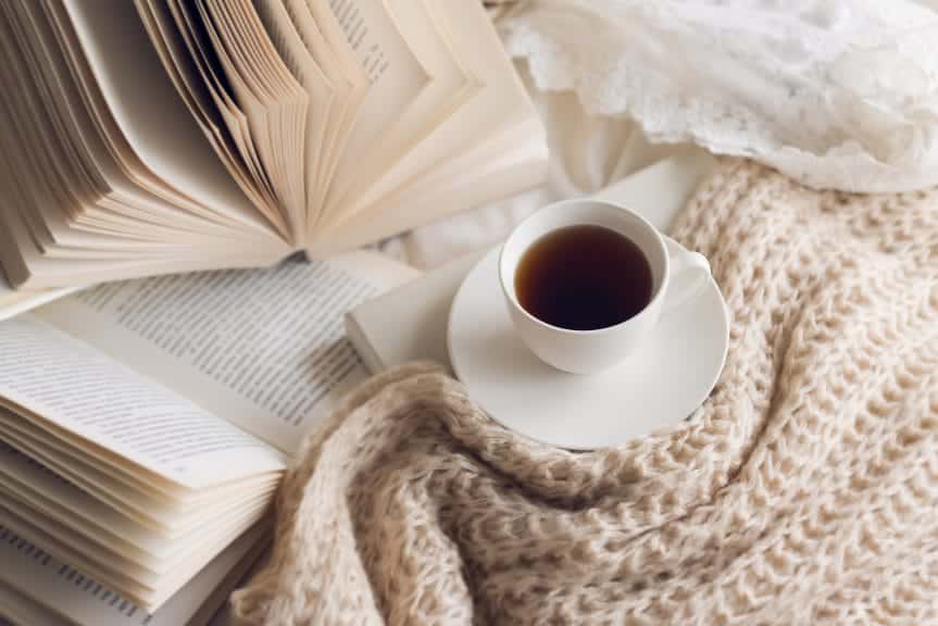 Many books on the bed and a cup of coffee.