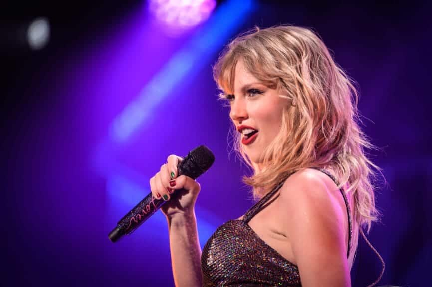 Taylor Swift singing a song on stage with a mike in hand.