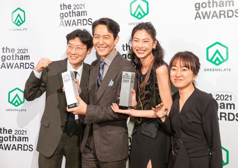 Two Korean men and women in grey suits and black dresses holding two awards shaped like white columns