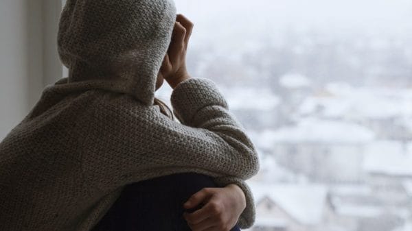 Sad teen girl looks out the window back to the camera.