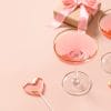 Festive champagne, romantic gift and two pink lollipops on stick on pink background. Galentine's day greeting card. Close up.