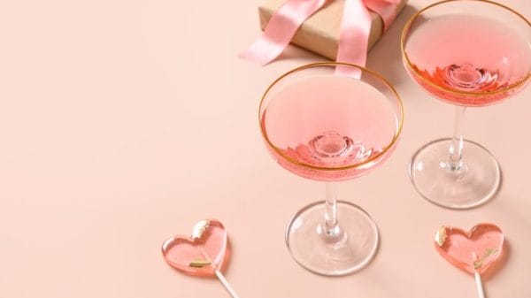 Festive champagne, romantic gift and two pink lollipops on stick on pink background. Galentine's day greeting card. Close up.