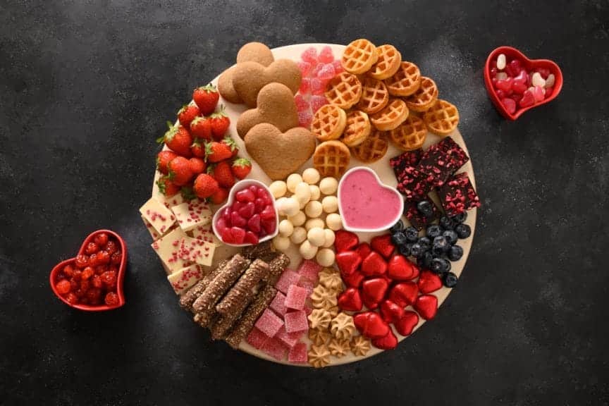 Galentines Day charcuterie sweet board with chocolate, different snacks, berries and cookies on black background. View from above.