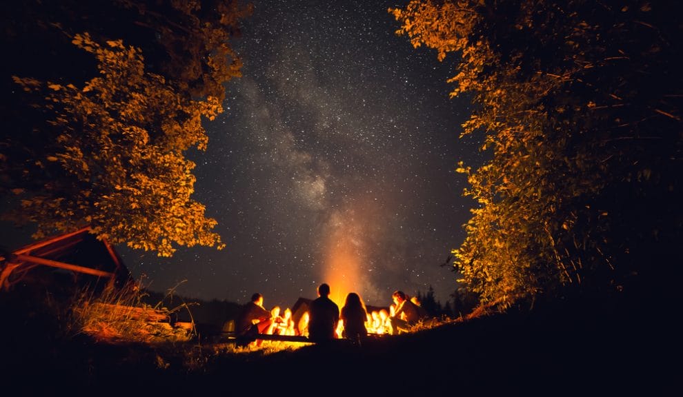 Campfire at night under the stars with group of people around.