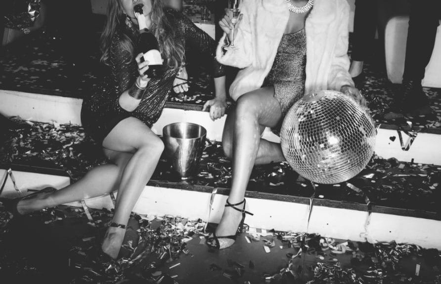 Two girls sitting on a staircase littered with confetti in a party.