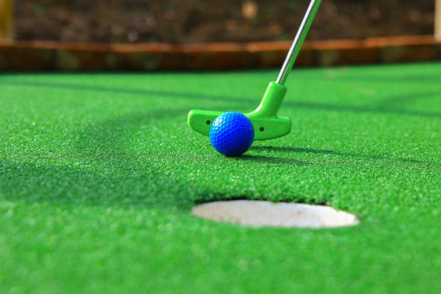Green putter hitting a blue ball on a mini golf course