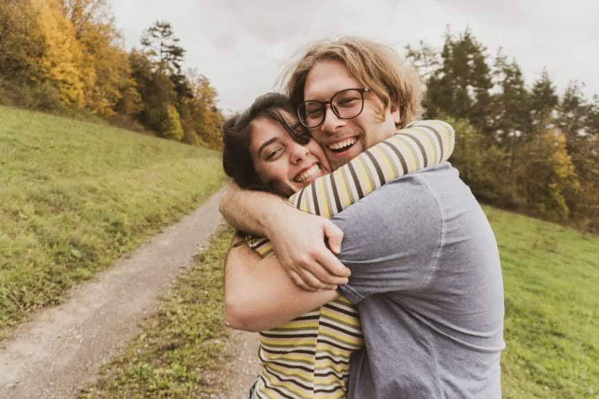 Two people hugging outside next to a pathway.