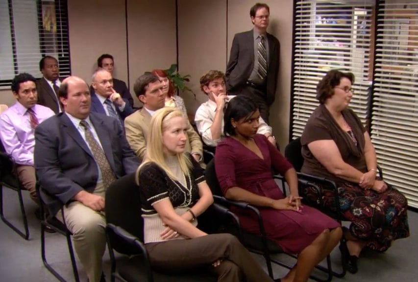 The Dunder Mifflin Scranton employees are gathered for a meeting in the conference room.