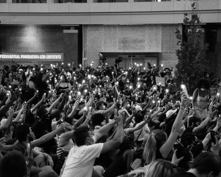 A crowd of people during a protest on the street, holding phones with flashlights on.