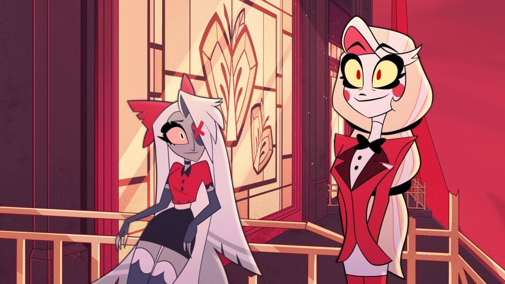 Charlie, a tall blonde demon woman stands on the balcony with her girlfriend Vaggie, a demon with grey skin and white hair