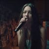 Olivia Rodrigo sings into a microphone within a darkened room.