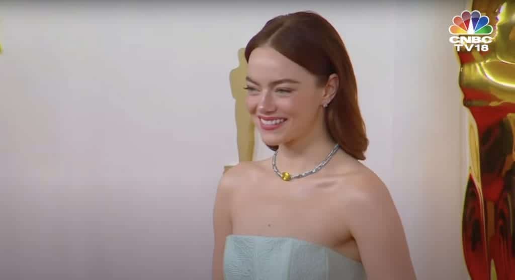 Emma Stone smiles in a light blue dress with a silver necklace on the Oscars red carpet. 