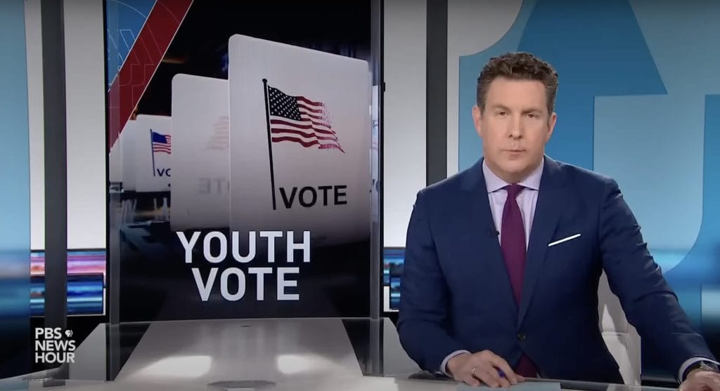 Screen with "Youth Vote" is on the left with an American flag and the word "Vote" underneath it above the words. Man in a blue suit with a purple tie sits to the right of the screen. 