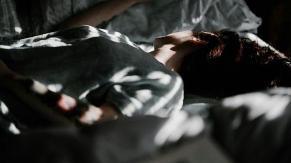 A person lying down on their bed in a dark atmosphere with sunlight spots scattered randomly.