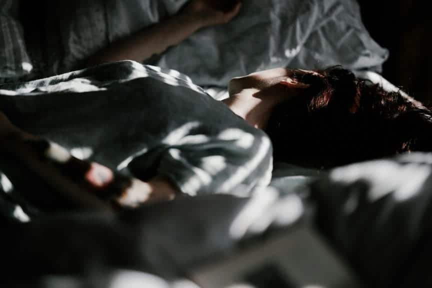 A person lying down on their bed in a dark atmosphere with sunlight spots scattered randomly.