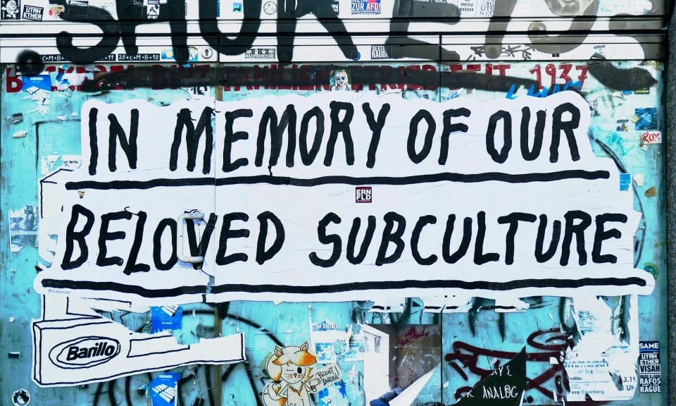 A graffitied wall with the text 'In memory of our beloved subculture'