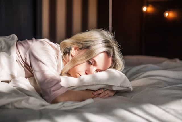 A sad woman laying on her bed.