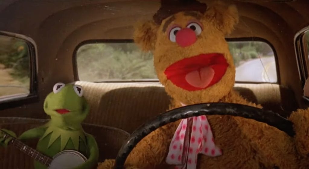 The image shows Muppets Kermit the Frog and Fozzie Bear singing and playing the banjo as they drive along a country road.