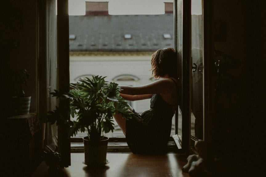 Girl sitting by an open window gazing out with her head away from the camera. Getting over a situationship. 