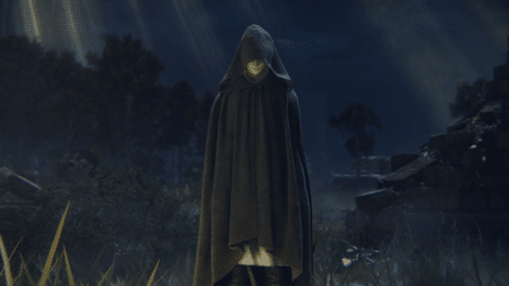 A hooded woman stands before a small golden bonfire.