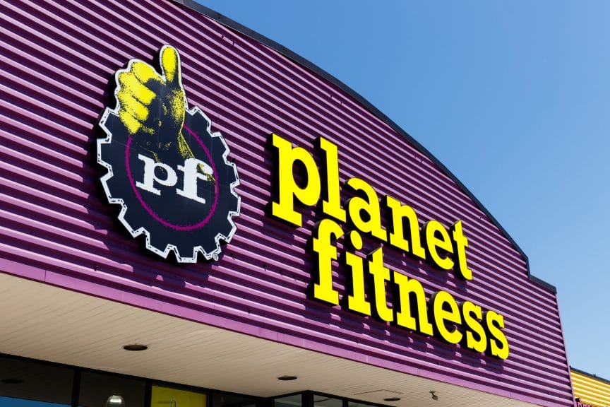 A purple striped building under a blue sky with the words planet fitness in yellow. The logo is a cog with the letters 'pf' on them below a yellow thumbs up