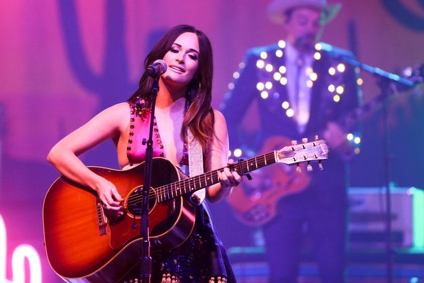 Kacey Musgraves performing live on stage at the Paramount in Huntington, NY on July 18, 2015. Musgraves, a country musician, is seen under bright stage lights, engaging the audience with her music and presence.