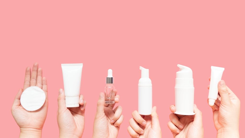 Six skincare products in hands in front of a pink background.