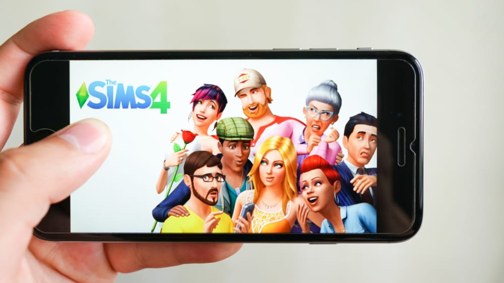A hand holding a phone with the sims 4 logo 