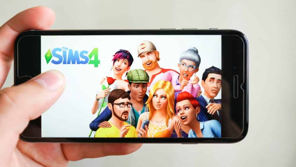 A hand holding a phone with the sims 4 logo