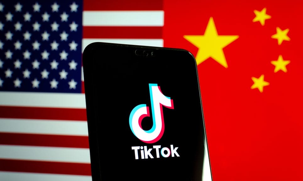 Phone with TikTok logo pictured in front of American and Chinese flags