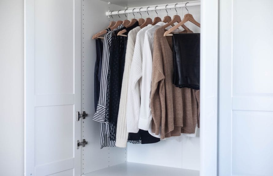 Picture shows a white wardrobe with clothes hanging on hangers.