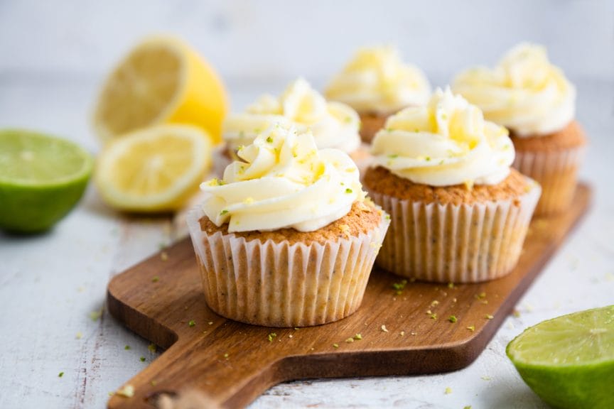 The image shows lemon cupcakes on a wooden cutting board.
