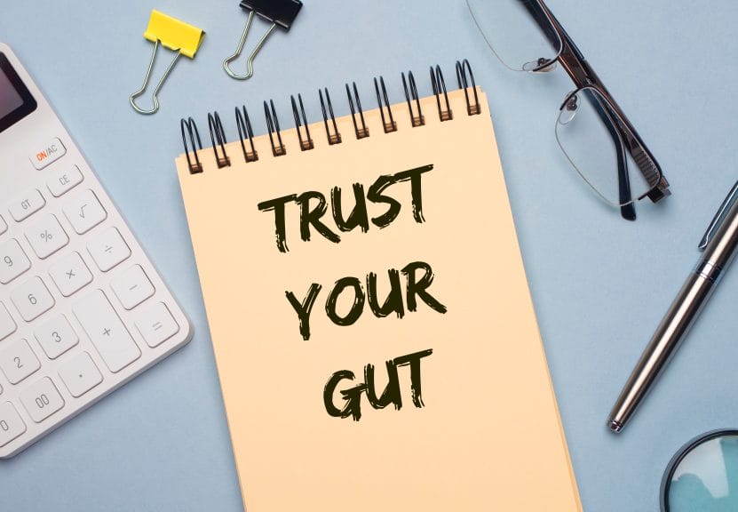 A notepad that states, "Trust your gut" on it, with some office supplies surrounding the pad.