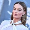 Margot Robbie on a red carpet wearing a white dress straight hair pulled behind her ears.