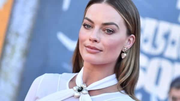 Margot Robbie on a red carpet wearing a white dress straight hair pulled behind her ears.