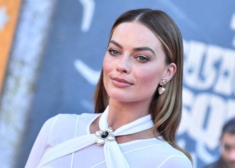 Margot Robbie on a red carpet wearing a white dress straight hair pulled behind her ears.