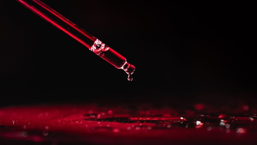 A pipette and a drop of red liquid, water, poison, acid, blood on a black background.