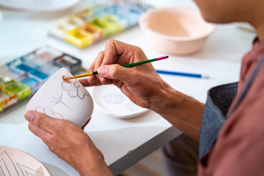 A person painting flowers on a white mug.