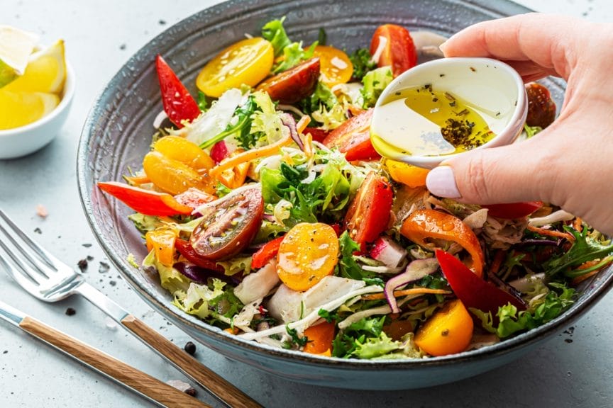 The image shows a colourful spring salat with a person pouring some dressing on top.