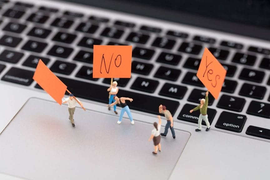 An image of a laptop keyboard with little figurines holding up orange post-its that read either "no" or "yes".