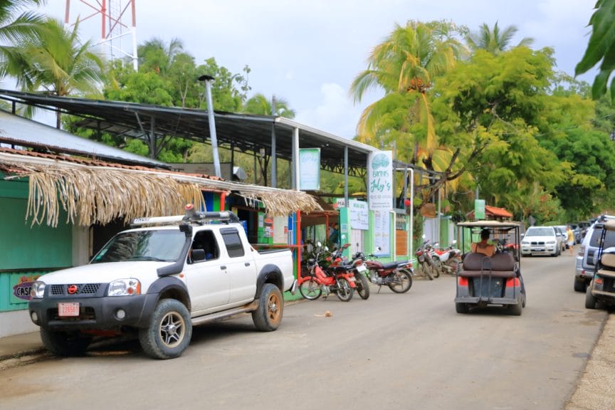 Small village in Guanacaste, Nicoya in Costa Rica. A street with cars and bikes, and a small building and trees in the background.