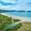 A sandy beach surrounded by forests and mountains in the background.