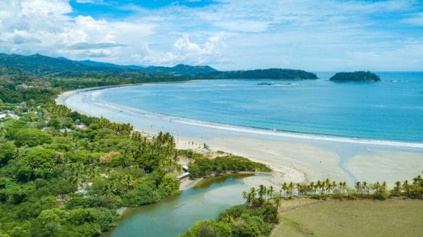 A sandy beach surrounded by forests and mountains in the background.