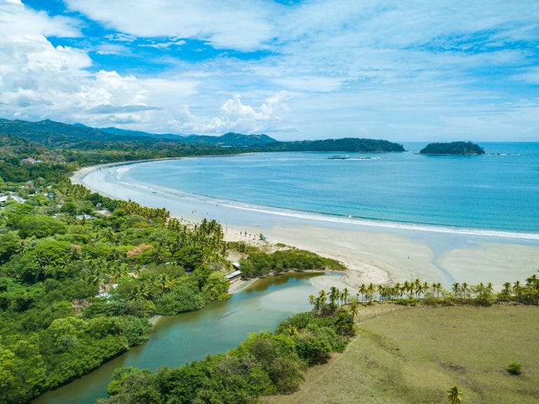 A sandy beach surrounded by forests and mountains in the background.