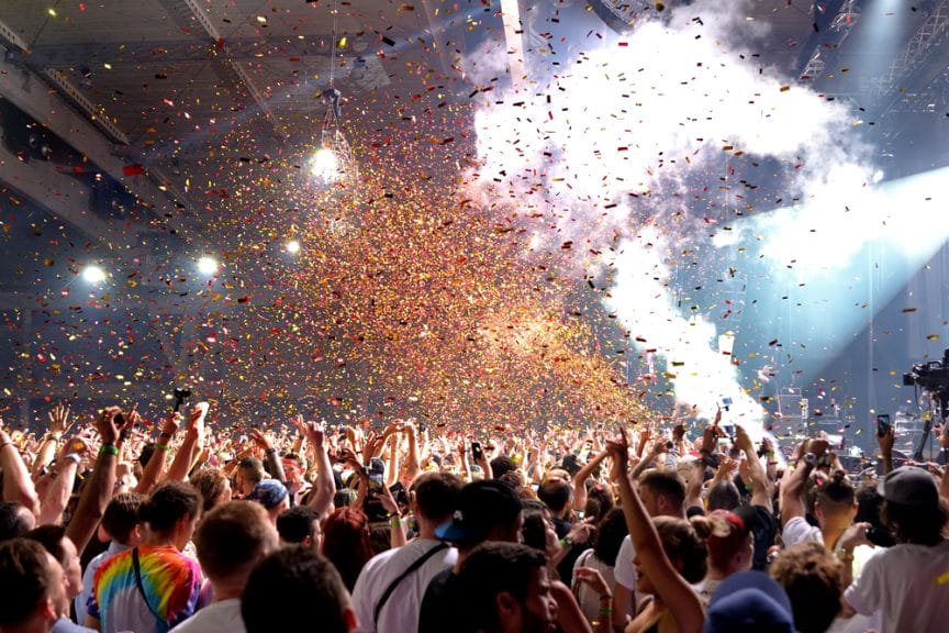 Crowd at a club with their hands up as confetti falls from the ceiling. 